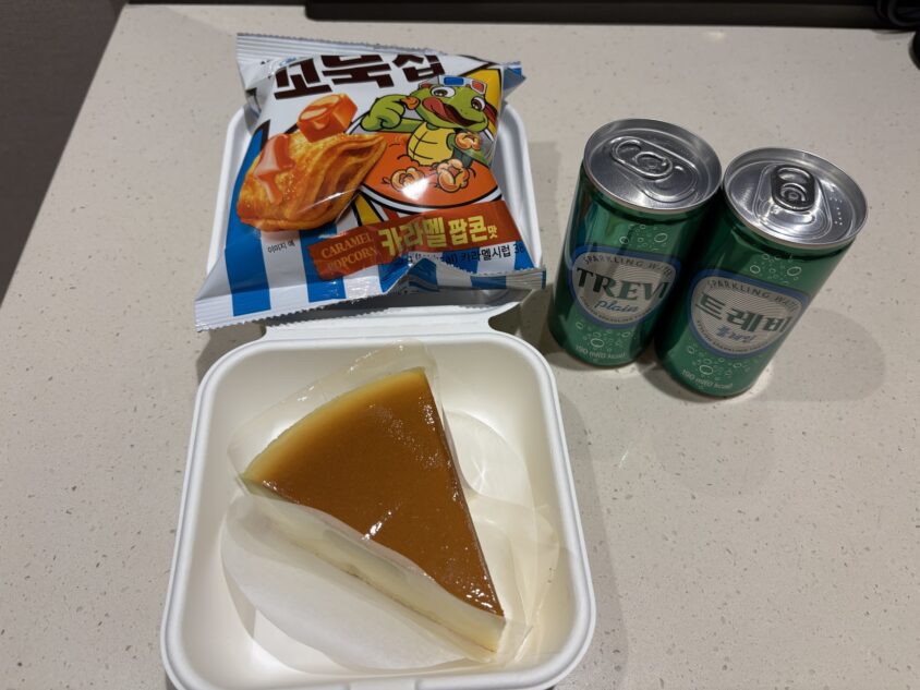 客室で受け取ったスライスチーズケーキと一緒に置かれた缶飲料・スナック